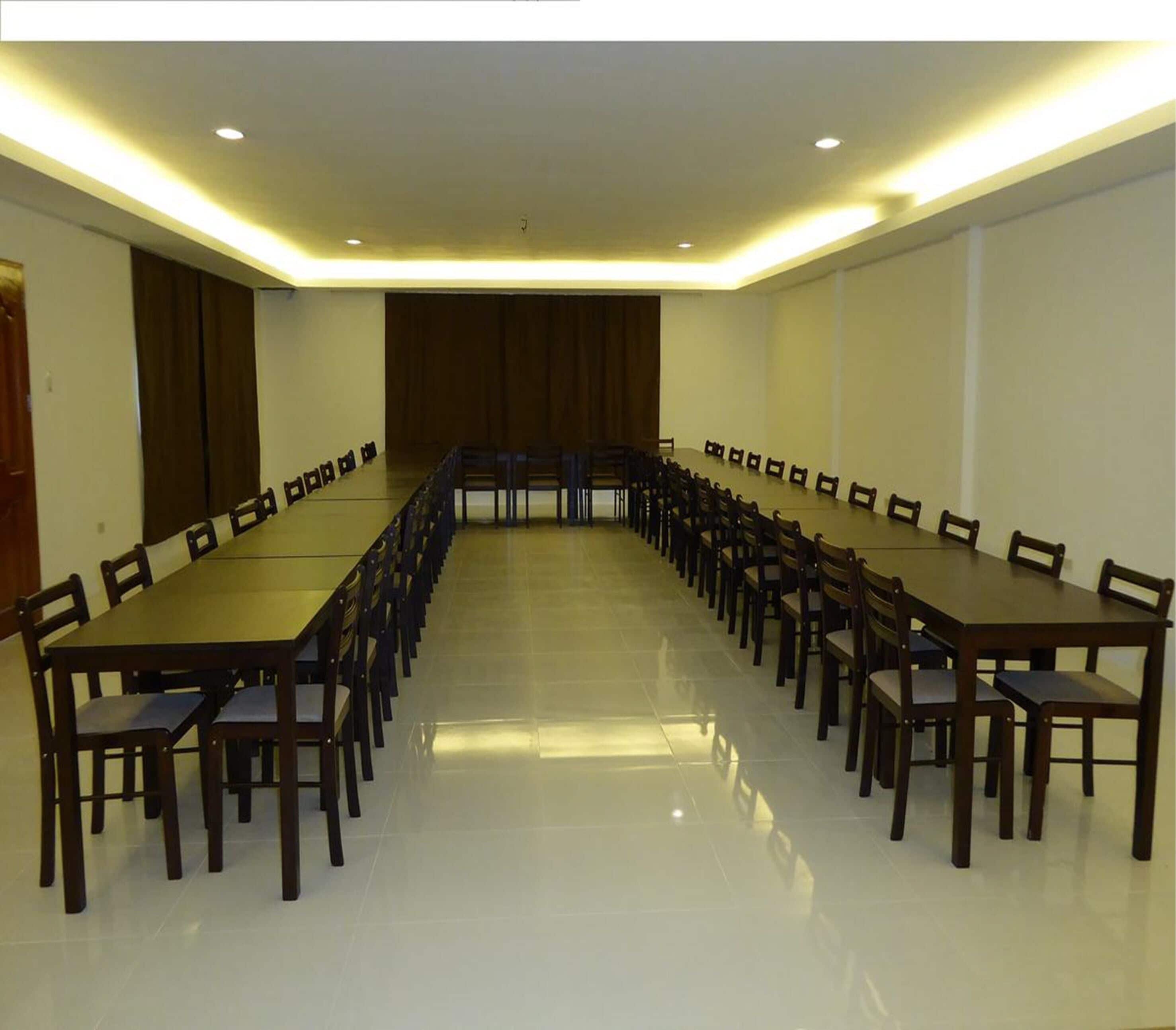 A conference room with a long table and chairs, recessed lighting, and a tiled floor.