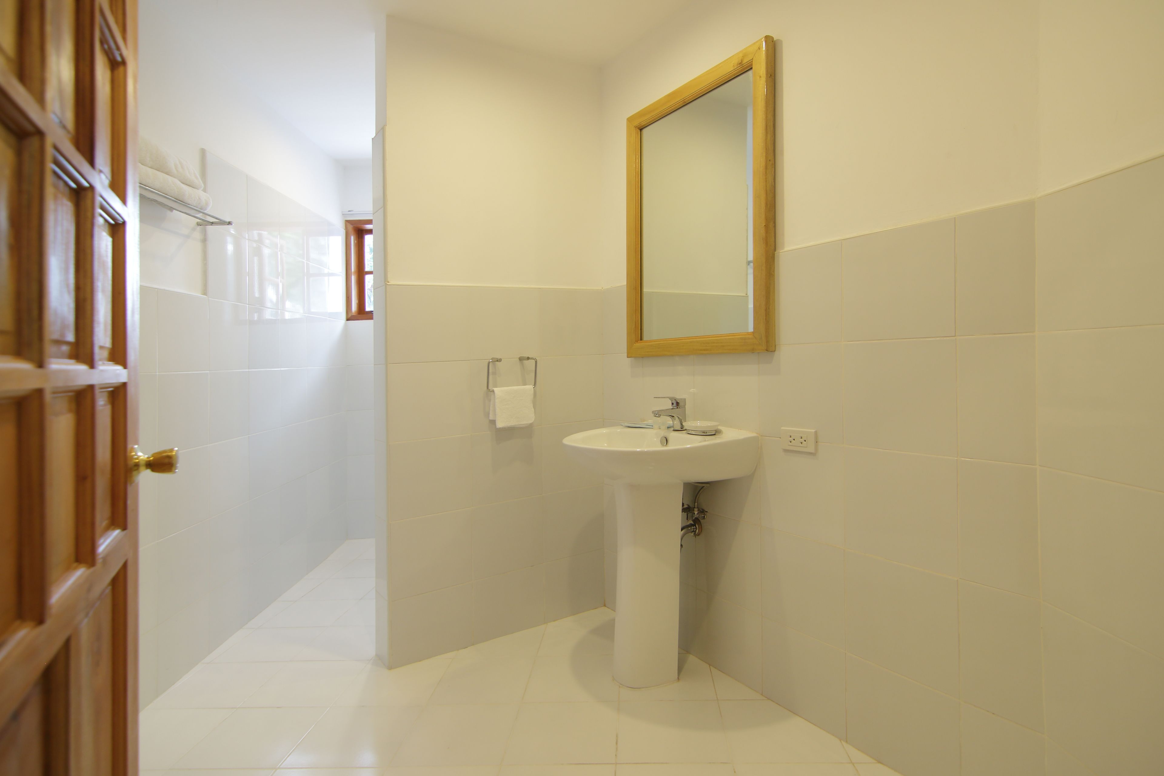 Une salle de bain avec un lavabo blanc, un miroir et une porte donnant sur une autre pièce.