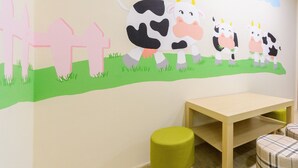 A children's room with a wall mural of cows, a wooden table, and two green stools. - Bryan Southern Villages (Tainan)