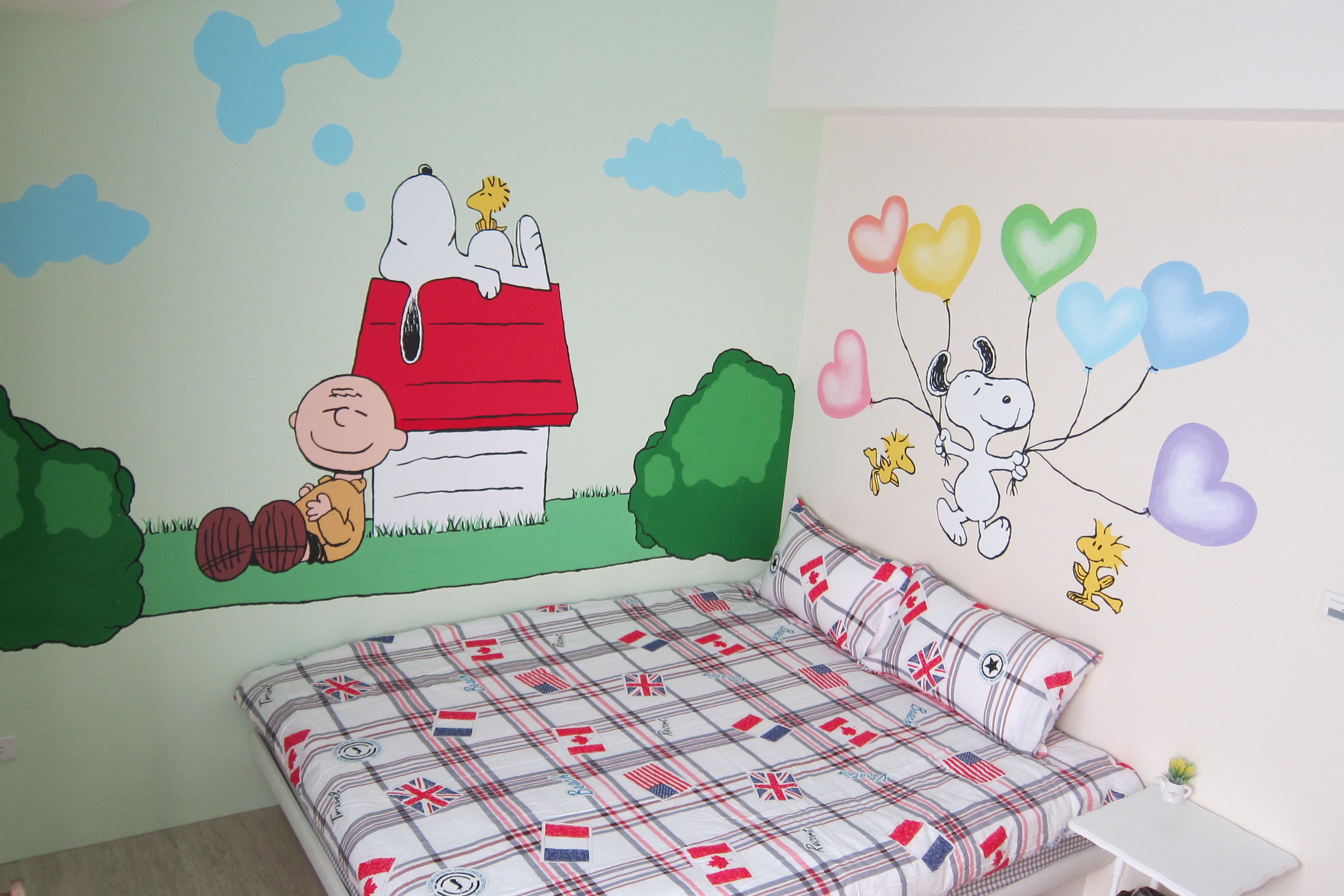 A bedroom with a bed, a wall mural, and a small table.