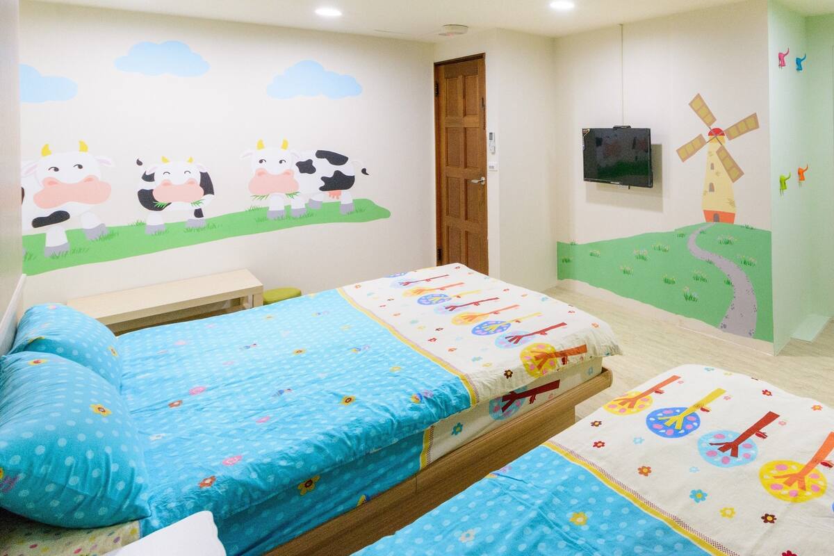 A child-friendly room with two beds, a TV, and playful wall decorations.