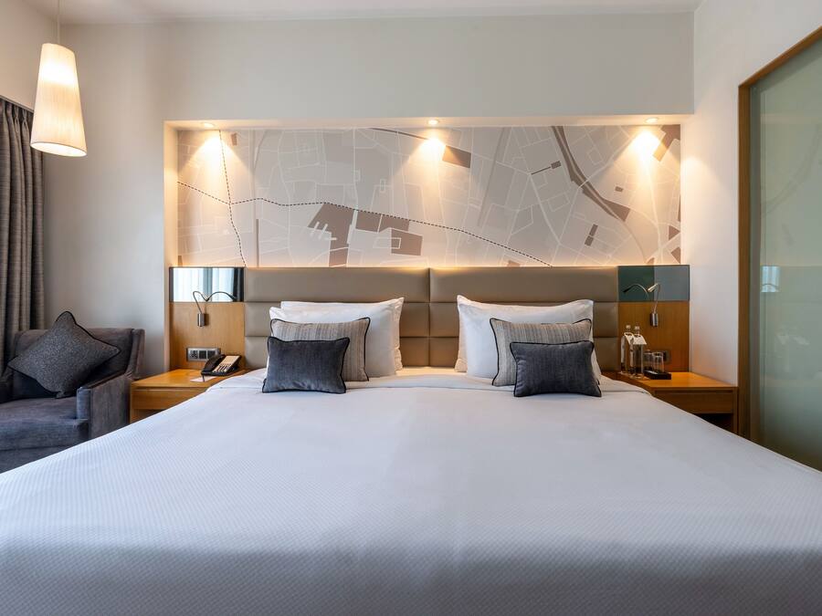 A hotel room with a large bed, a map on the wall, a chair, and a nightstand with a lamp.