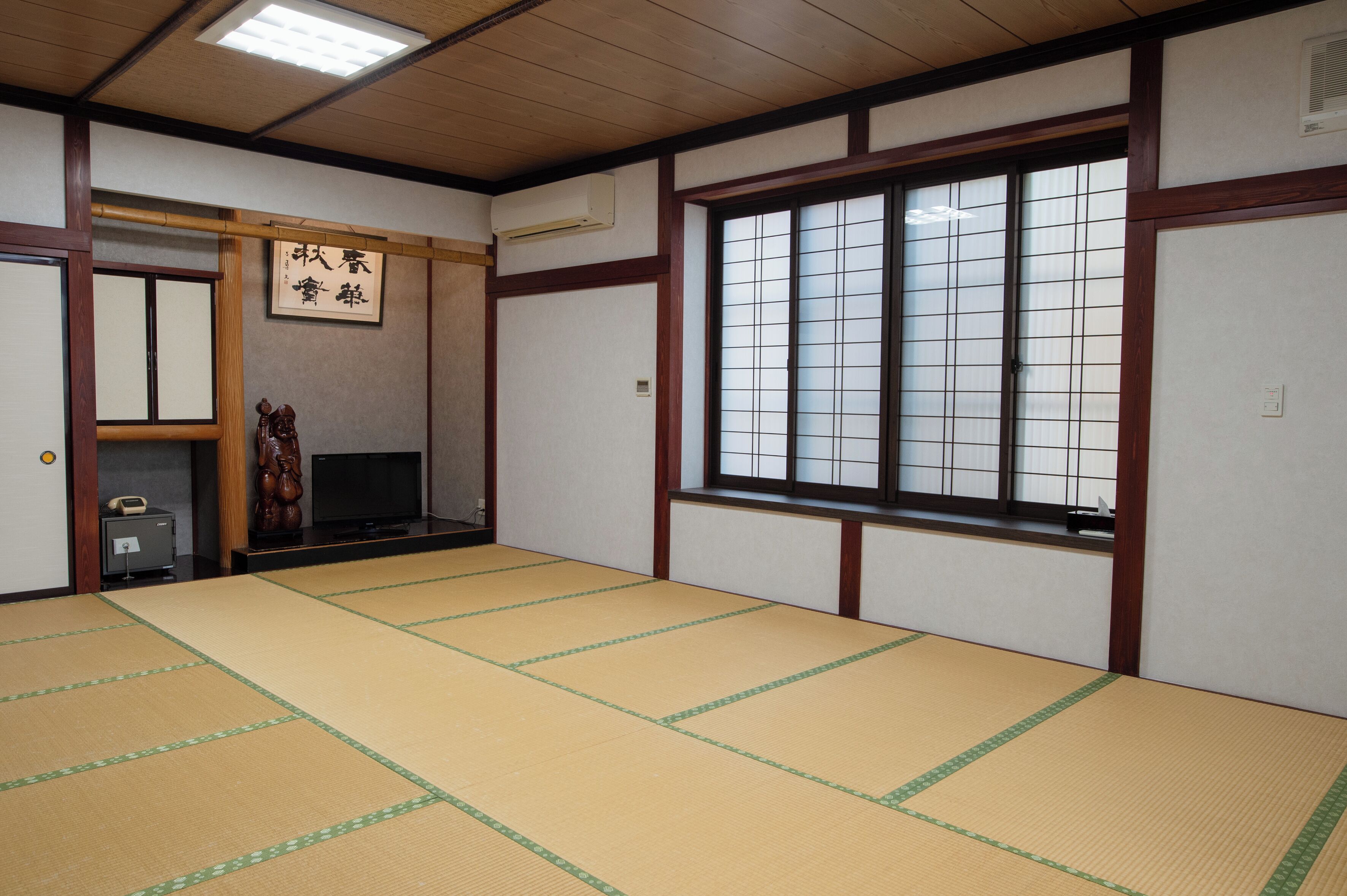 Una tradizionale stanza giapponese con pavimento in tatami, una porta scorrevole, un televisore e un'ampia finestra con persiane a griglia.