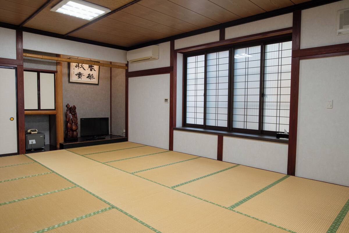 A traditional Japanese room with tatami flooring, a sliding door, a television, and a large window with grid panes.