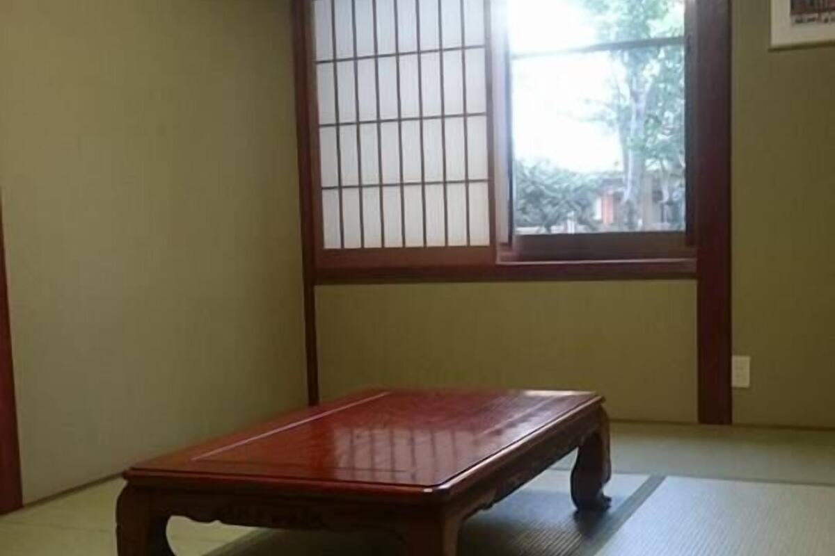 A tatami mat room with a wooden table, a shoji screen, and a window with a view of trees.