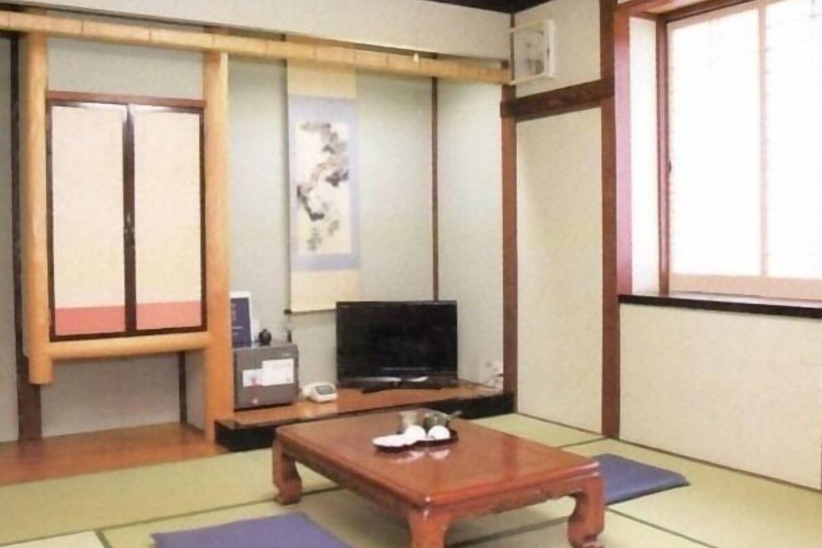A traditional Japanese room with tatami flooring, a wooden table, a television, and sliding doors.