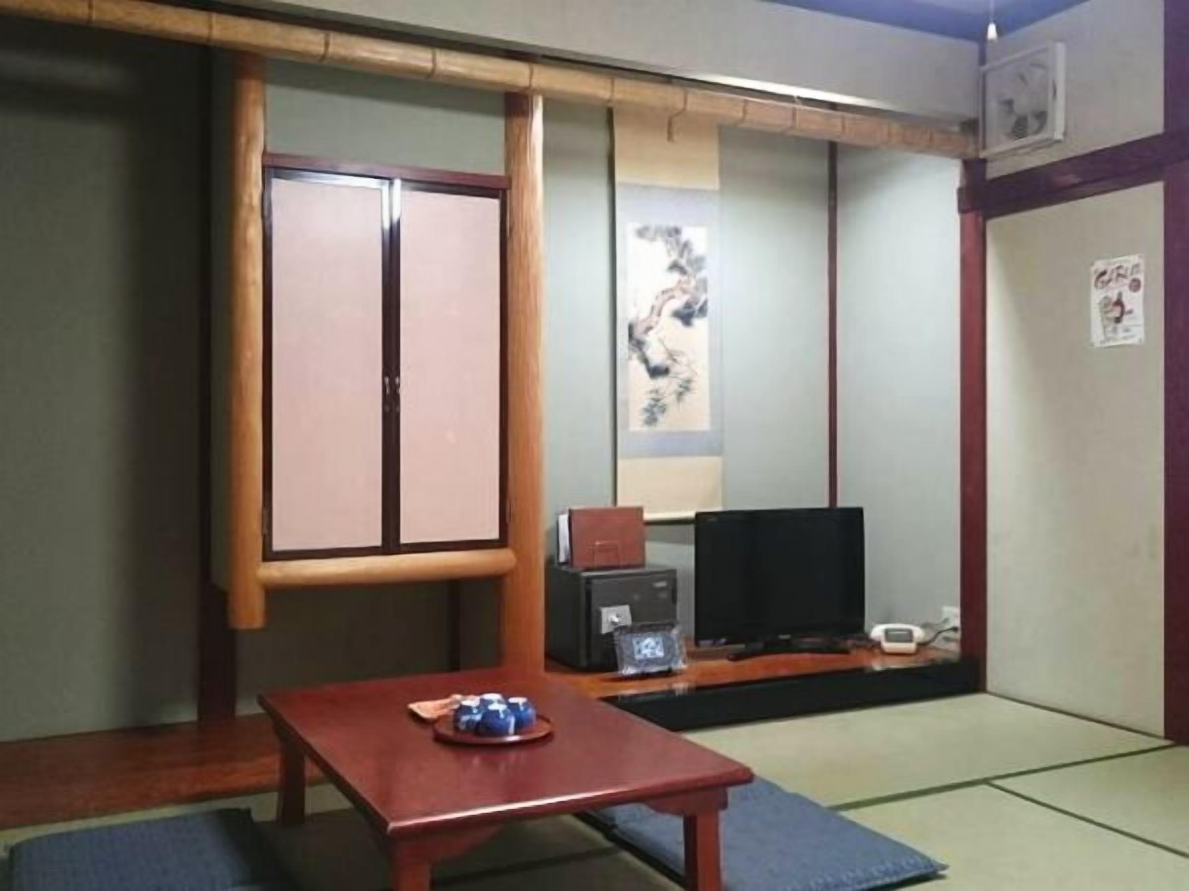 Una camera tradizionale giapponese con pavimenti in tatami, un tavolino in legno, una televisione e una porta scorrevole.