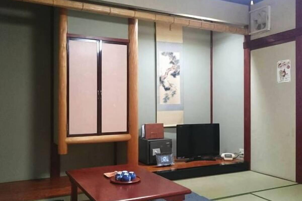 A traditional Japanese room with tatami flooring, a low wooden table, a television, and a sliding door.