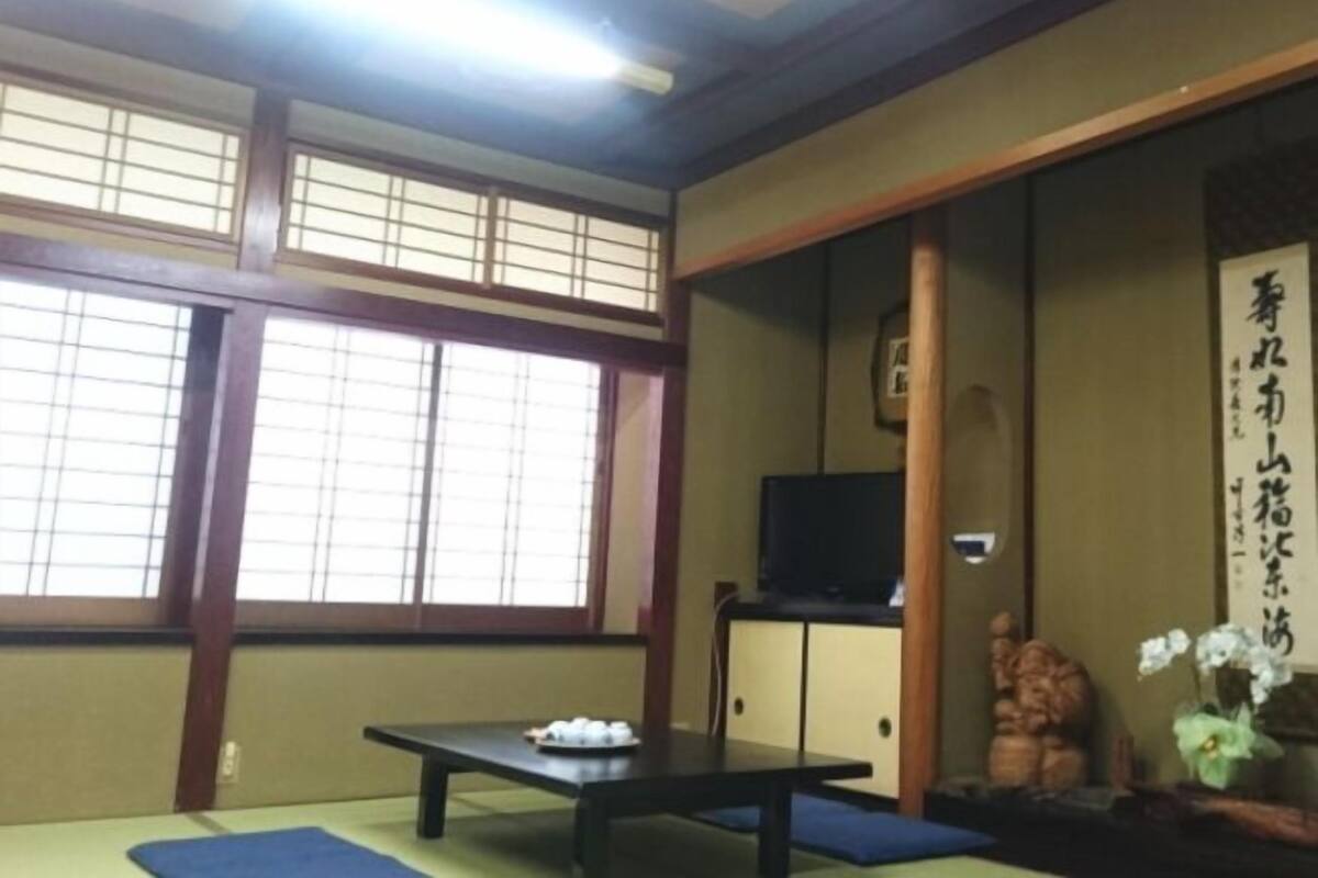 A traditional Japanese room with tatami flooring, a low table, a television on a cabinet, and a shoji screen.