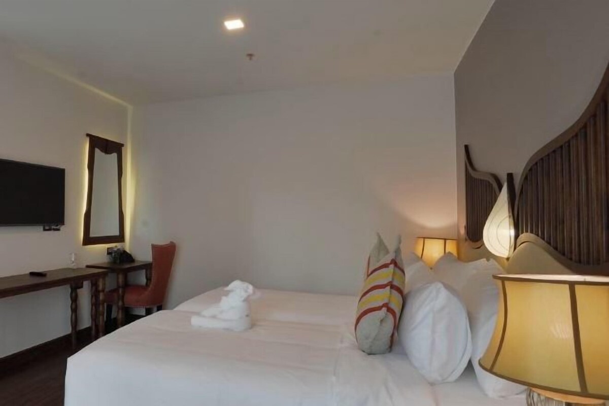 A hotel room with a bed, a desk, a chair, a television, and a lamp.