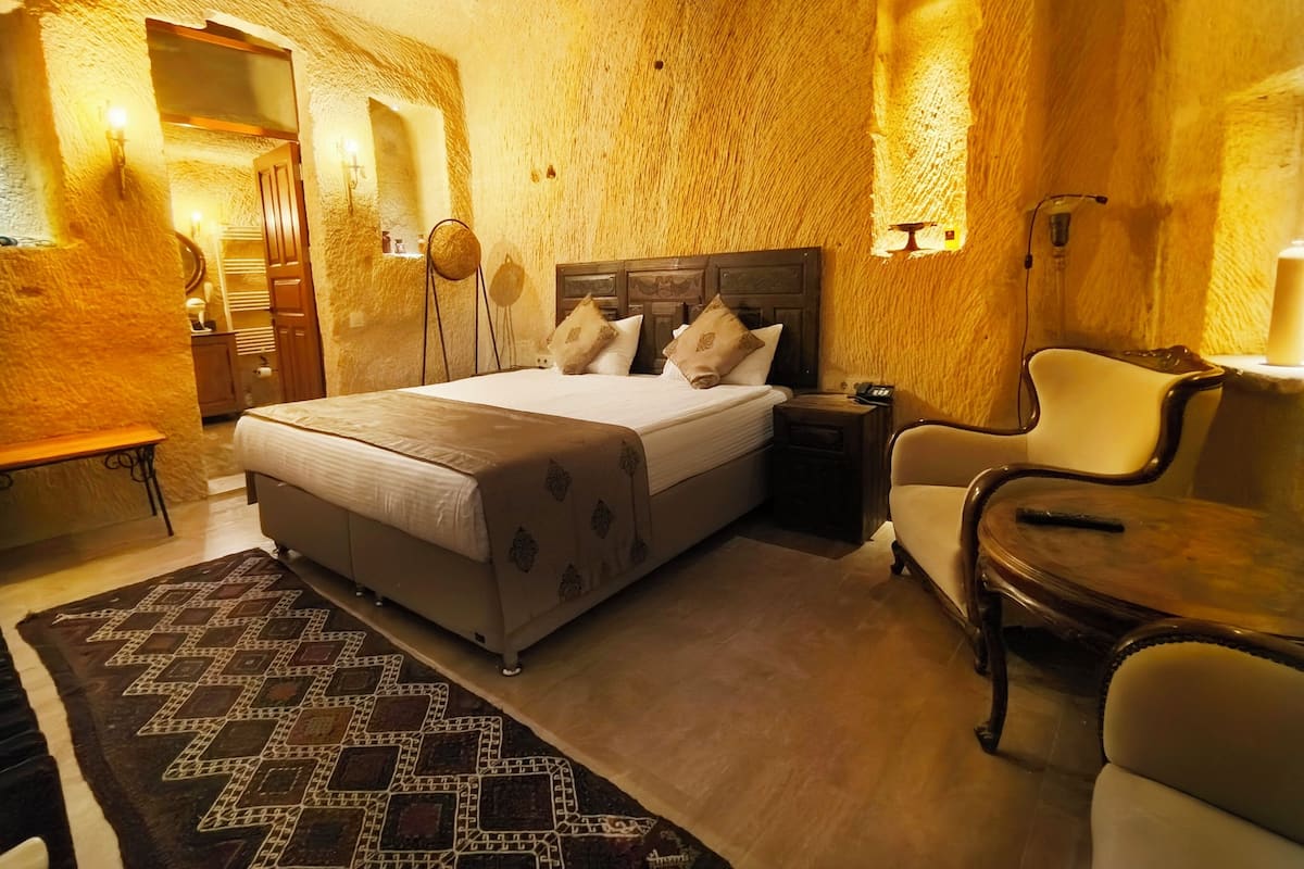 Una habitación acogedora con una cama grande, una mesita de noche de madera, una silla y una alfombra estampada.