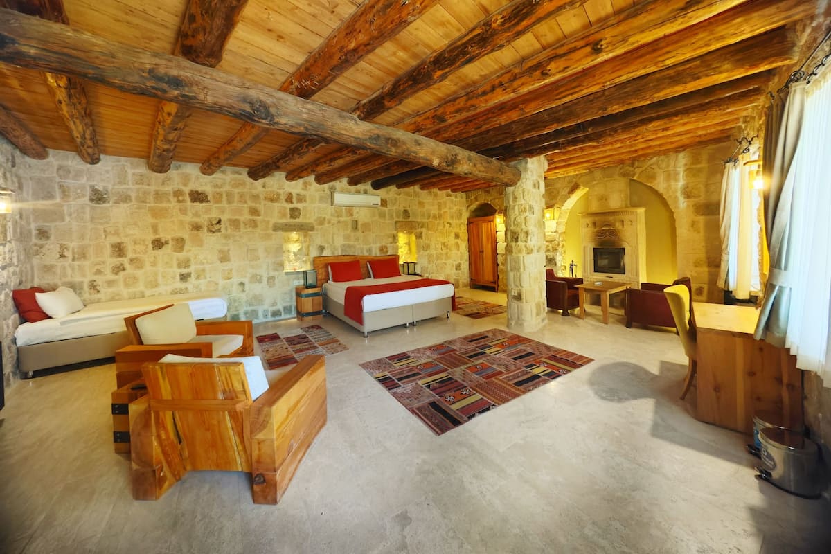 Una habitación rústica con paredes de piedra, techo de madera, cama, sofá y chimenea.