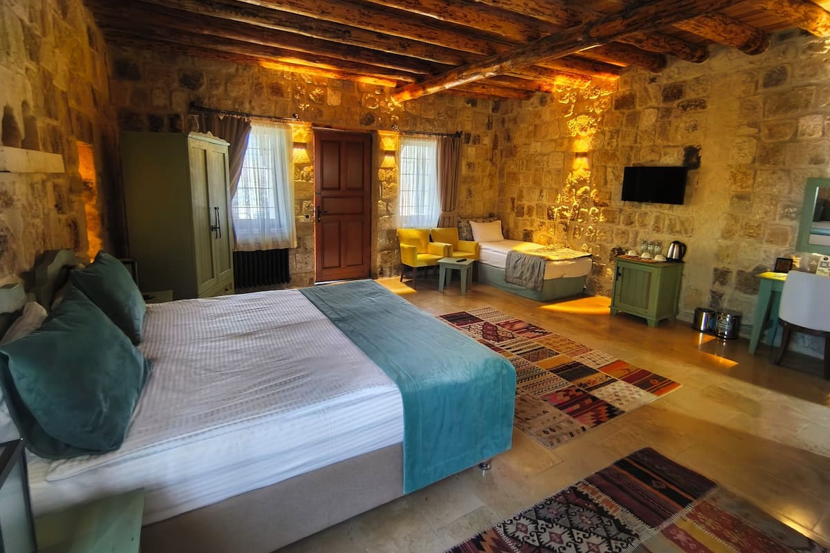 Un dormitorio rústico con cama, escritorio y silla. La habitación tiene paredes de piedra y vigas de madera en el techo.