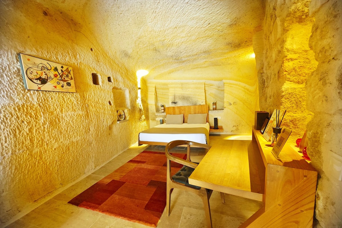 Un dormitorio acogedor, con forma de cueva, que incluye una cama, un escritorio de madera y una alfombra roja.