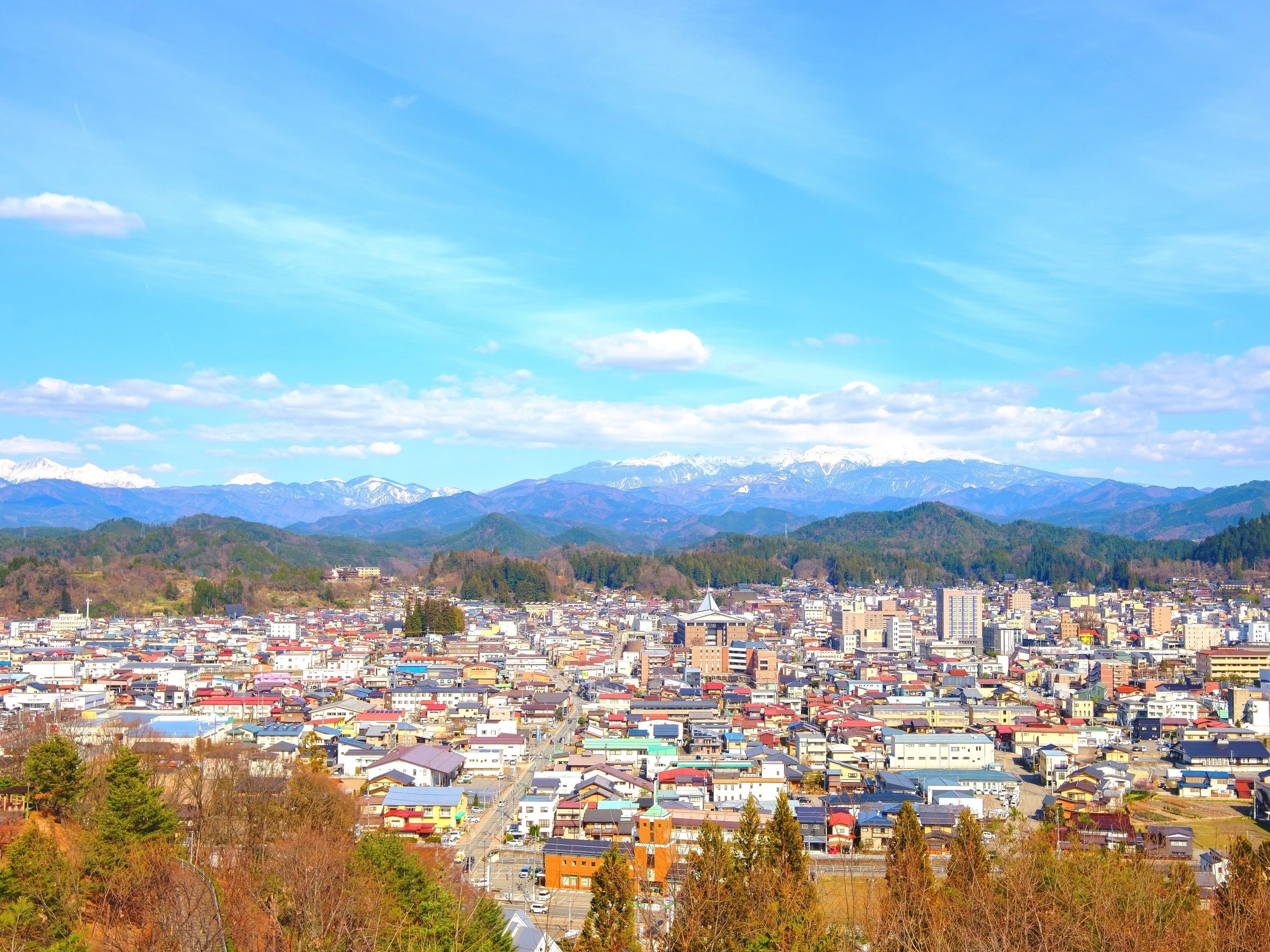 A panoramic view of a town with a dense cluster of buildings, a prominent church, and snow-capped mountains in the background.