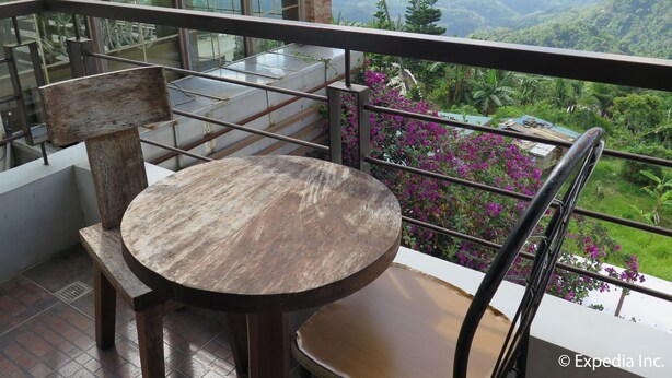 A balcony with a wooden table and chairs, overlooking a lush landscape with mountains and greenery. - The Windy Ridge Inn (Tagaytay)