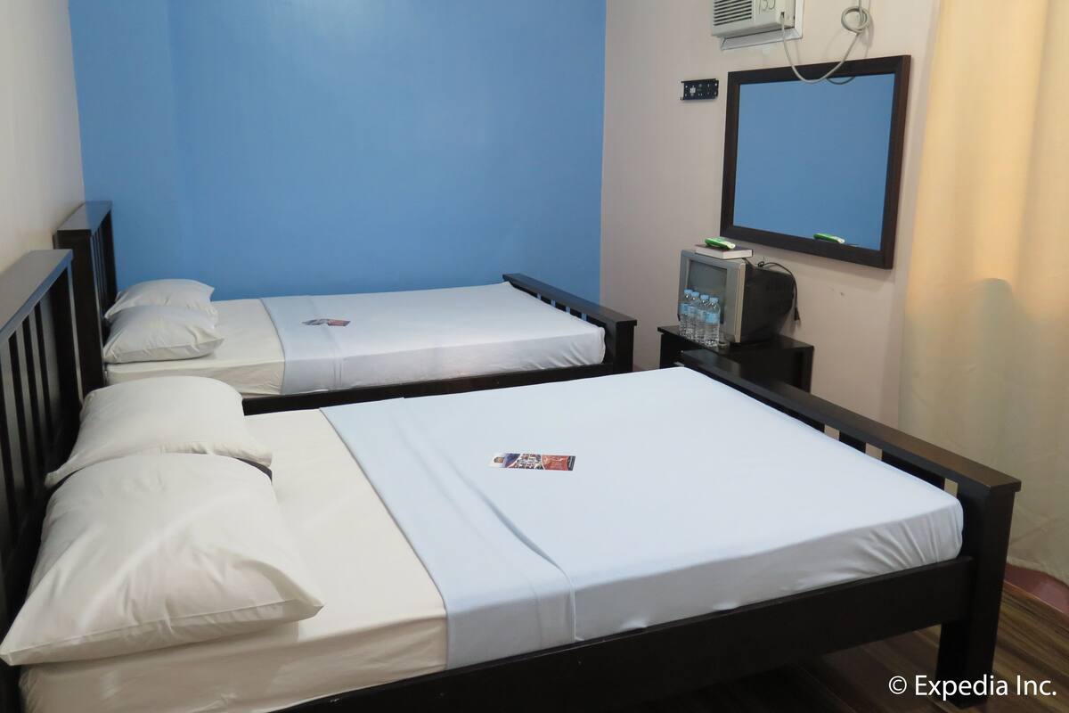 Habitación de hotel con dos camas individuales, un televisor pequeño y un equipo de aire acondicionado en la pared.