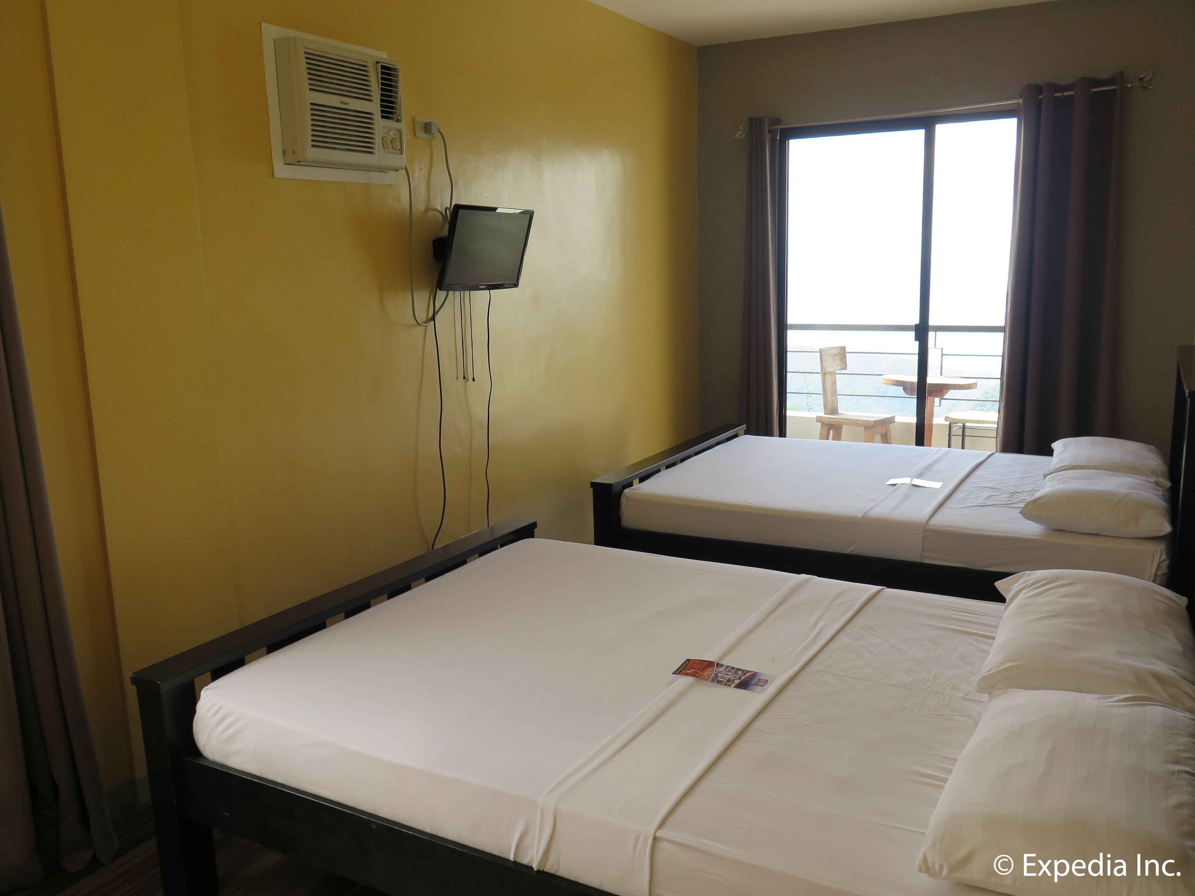 A hotel room with two beds, a TV mounted on the wall, and a window with curtains.