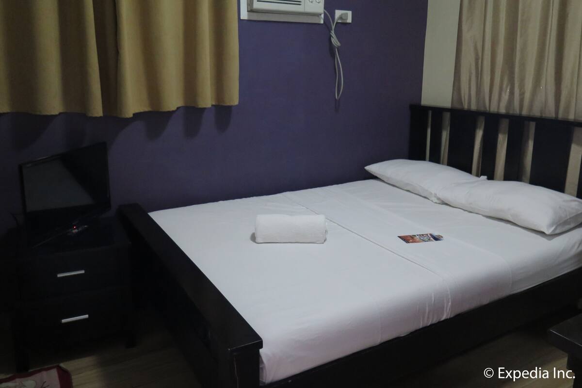 Una cama individual con ropa de cama blanca, una mesita de noche, una lámpara y un aire acondicionado instalado en la pared.