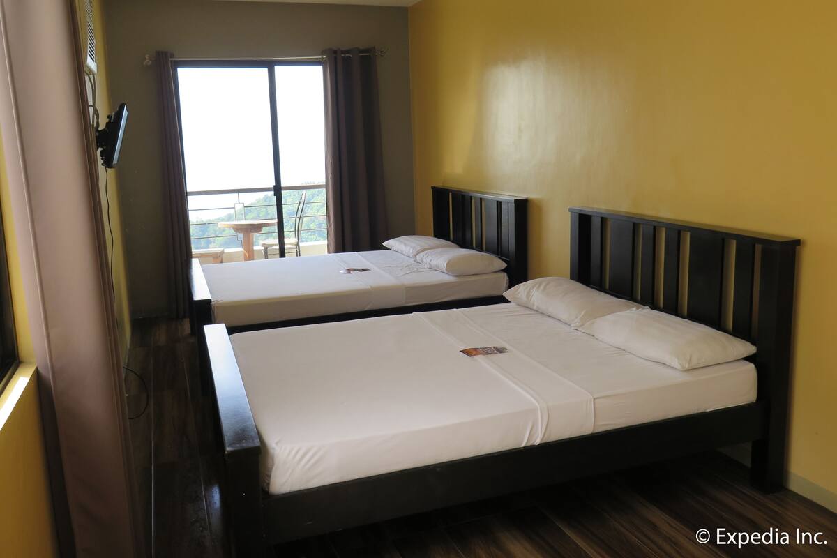 Habitación de hotel con dos camas, un balcón con mesa y sillas, y vistas al exterior.