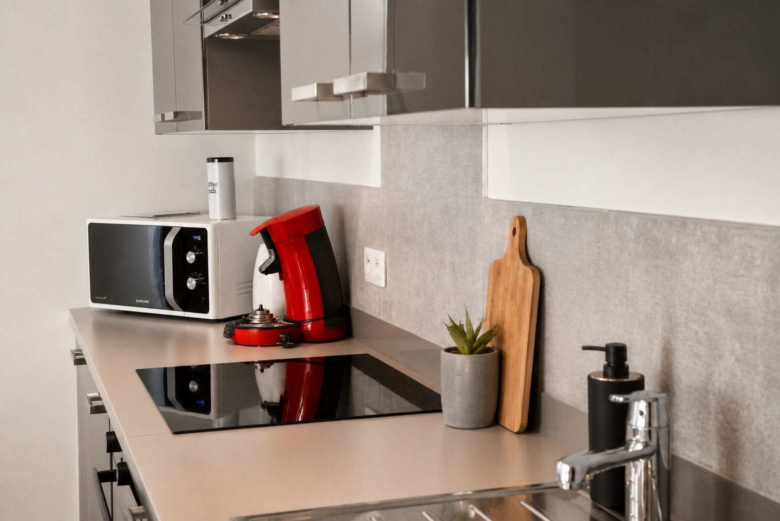 A modern kitchen with a microwave, coffee maker, and a small potted plant on the counter.