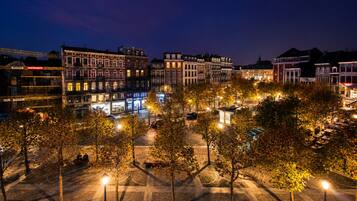 A nighttime cityscape with illuminated buildings and a tree-lined square.