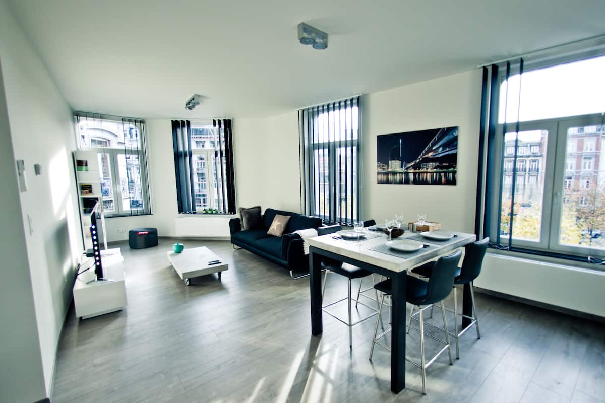 A modern living room with a dining area, large windows, and a city view.