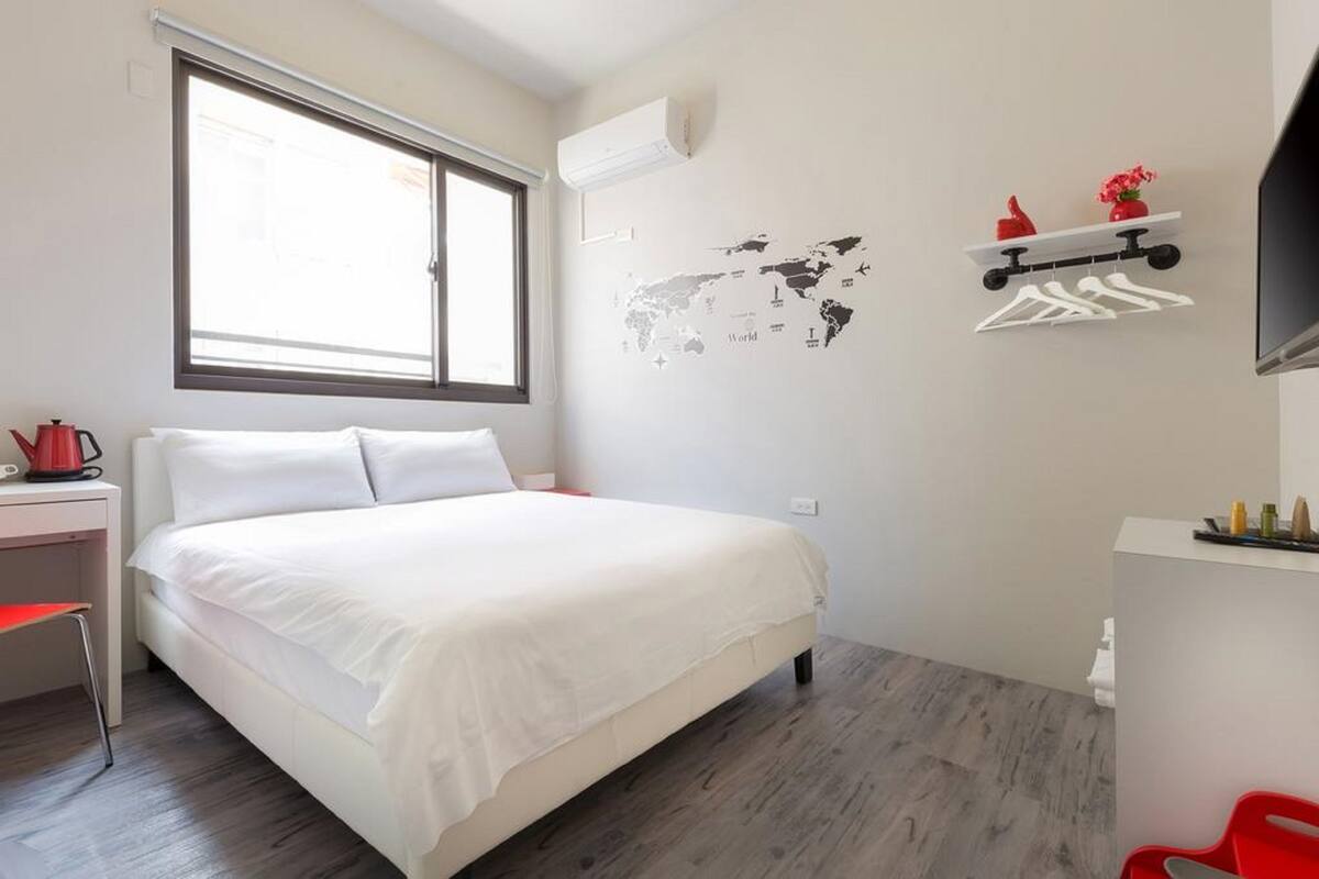 Un dormitorio con una cama grande, un escritorio, una silla, un mapa mundial decorando la pared y una estantería con objetos.