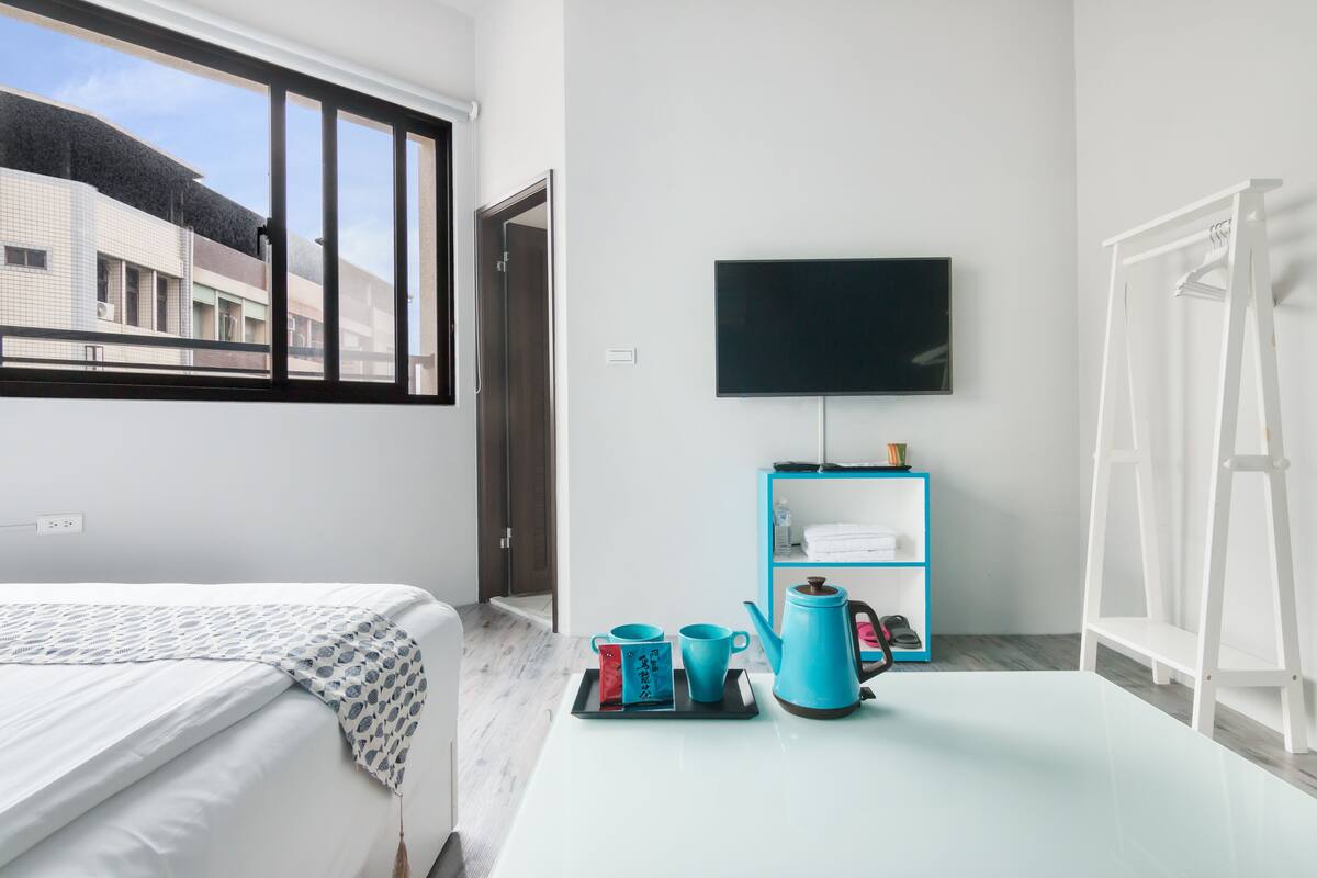 Una habitación de hotel con cama, televisión, cafetera y estante con toallas.
