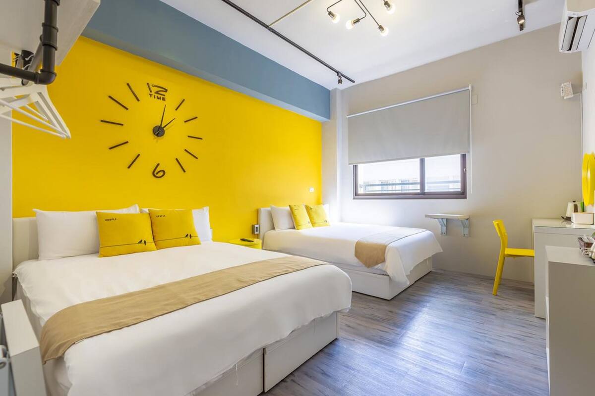 Habitación de hotel con dos camas, un reloj de pared grande, una ventana con vistas, un escritorio y una silla.