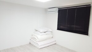A room with a stack of white pillows, a black window blind, and an air conditioning unit on the wall. - Amazon Guesthouse - Hostel (Seoul)