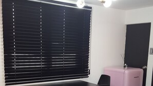 A modern kitchen with a black dining table, chairs, a pink refrigerator, and a window with blinds. - Amazon Guesthouse - Hostel (Seoul)