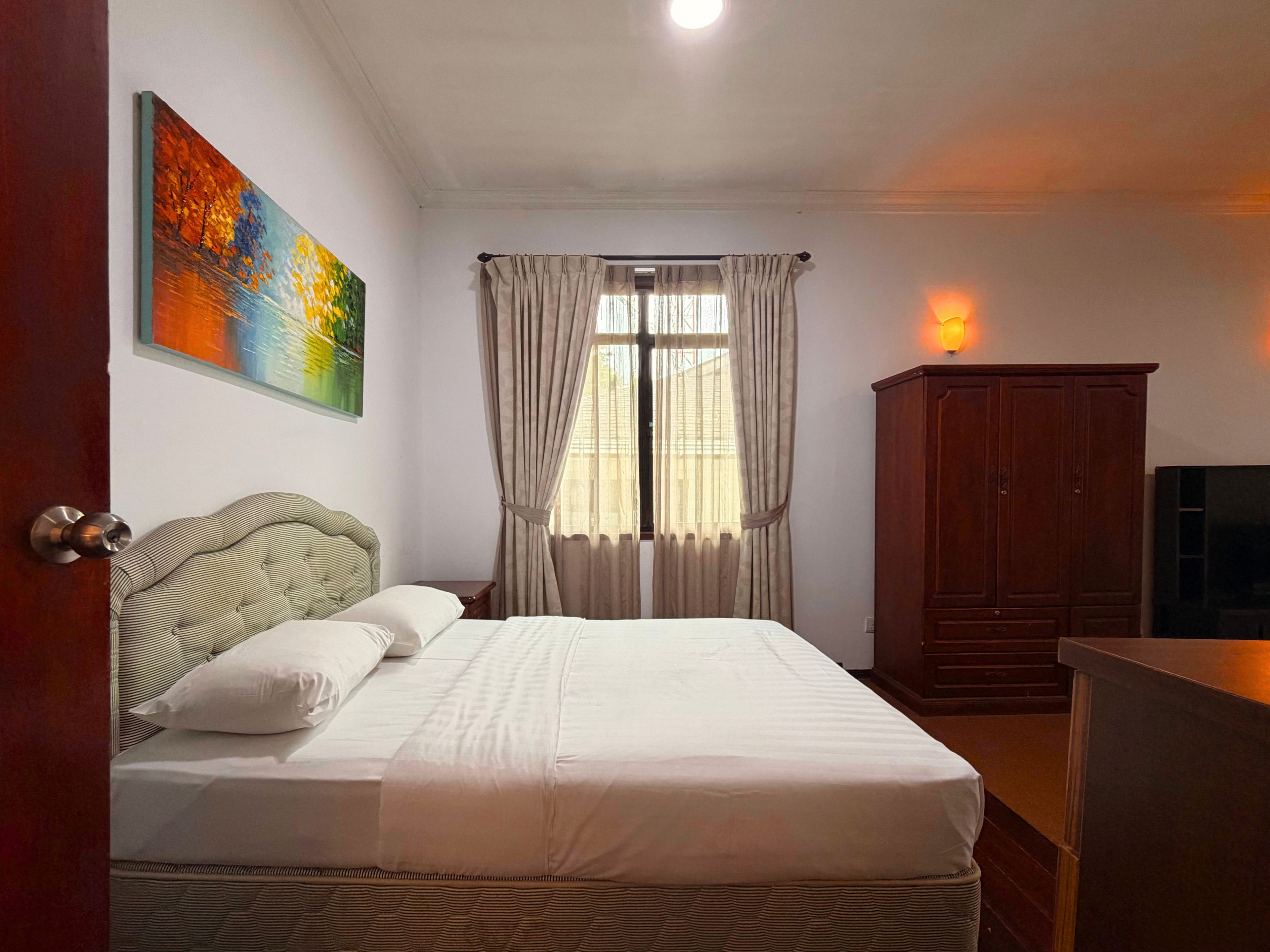 Una camera d'albergo con un letto, tende, un quadro, un armadio e una televisione.