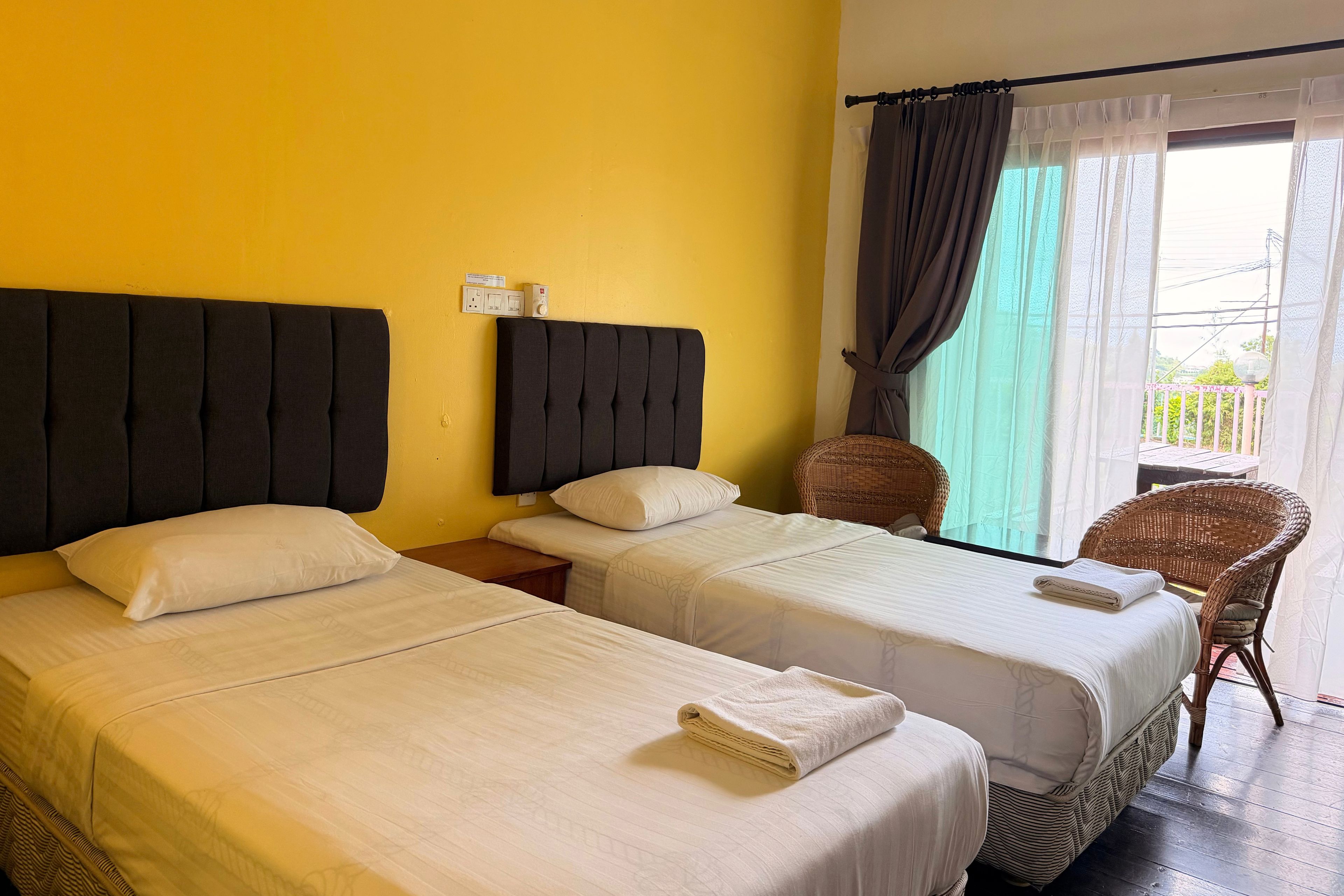 A hotel room with two beds, a window with curtains, a chair, and a view of the outdoors.