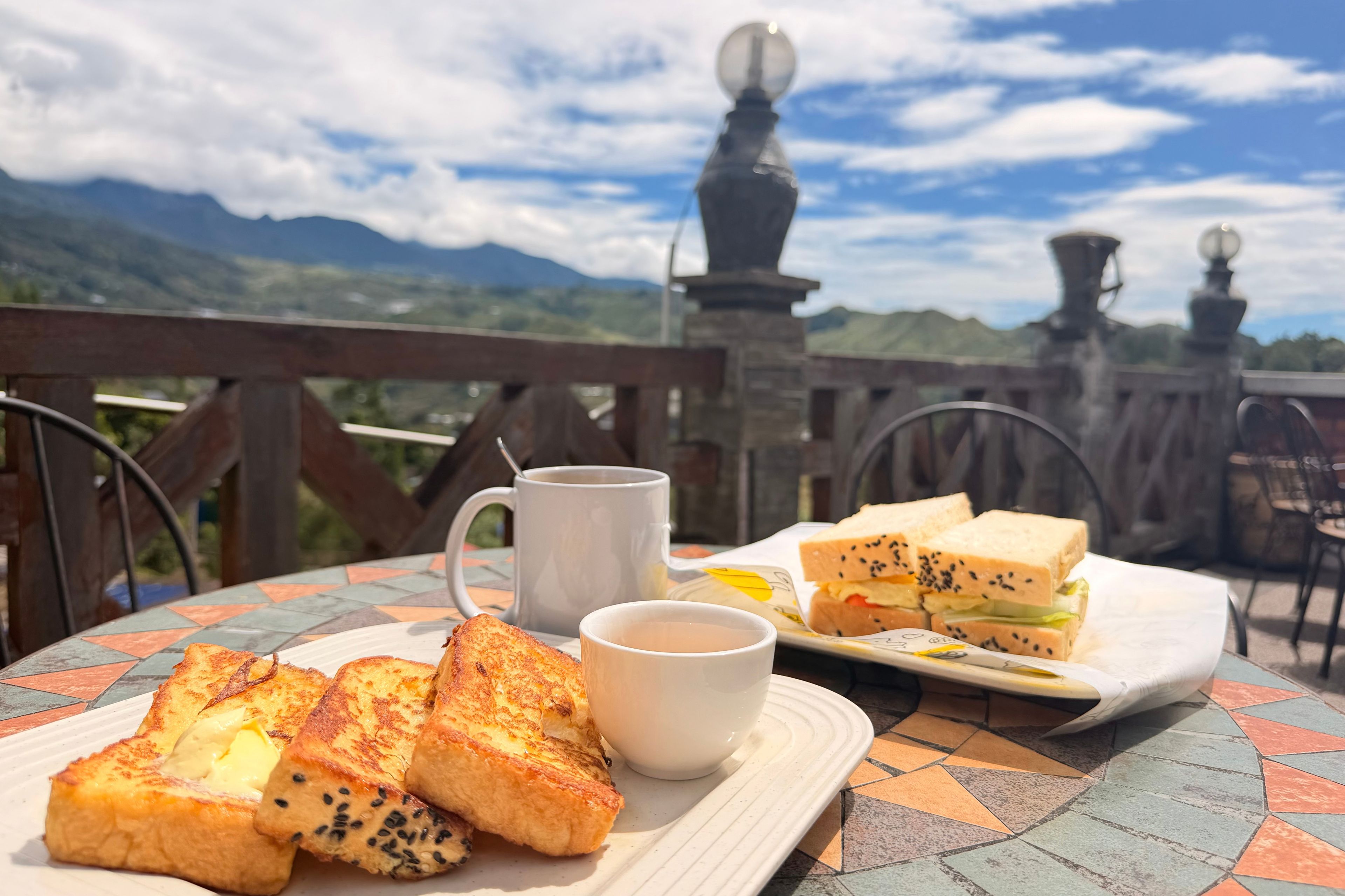 A table with toast, a cup of coffee, and a sandwich, set against a scenic mountain backdrop.