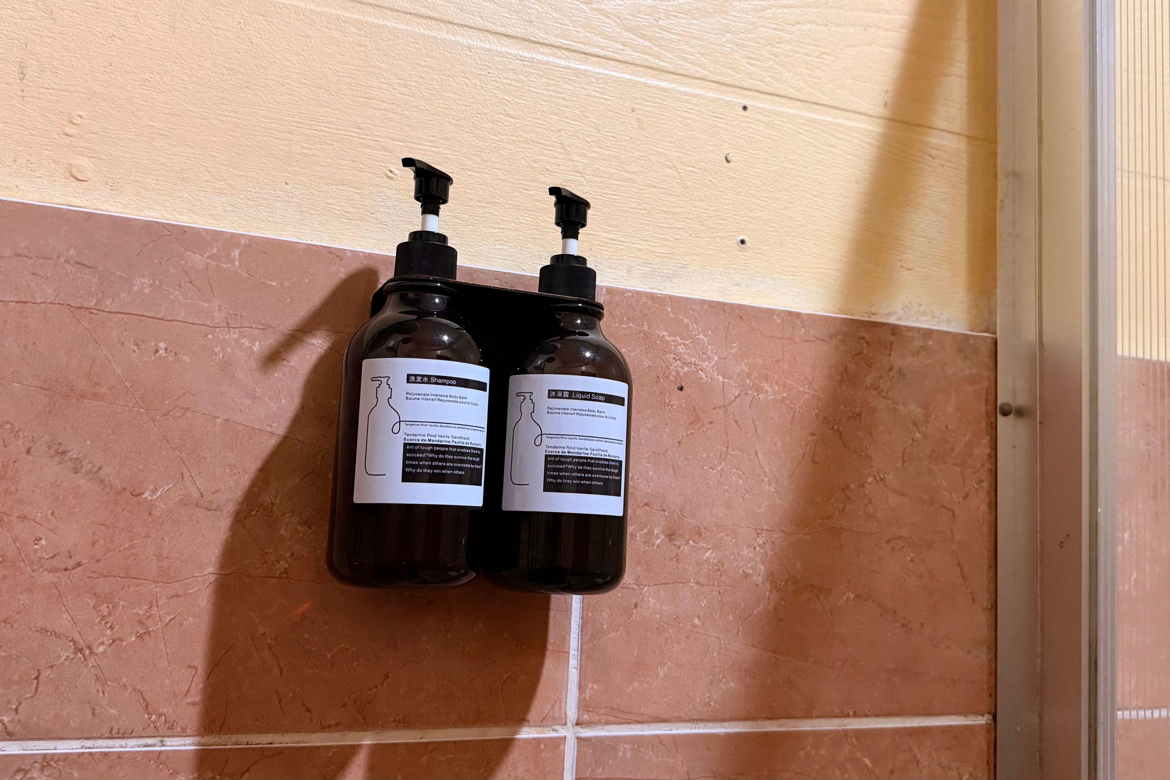 Two bottles of shampoo and liquid soap mounted on a tiled wall.