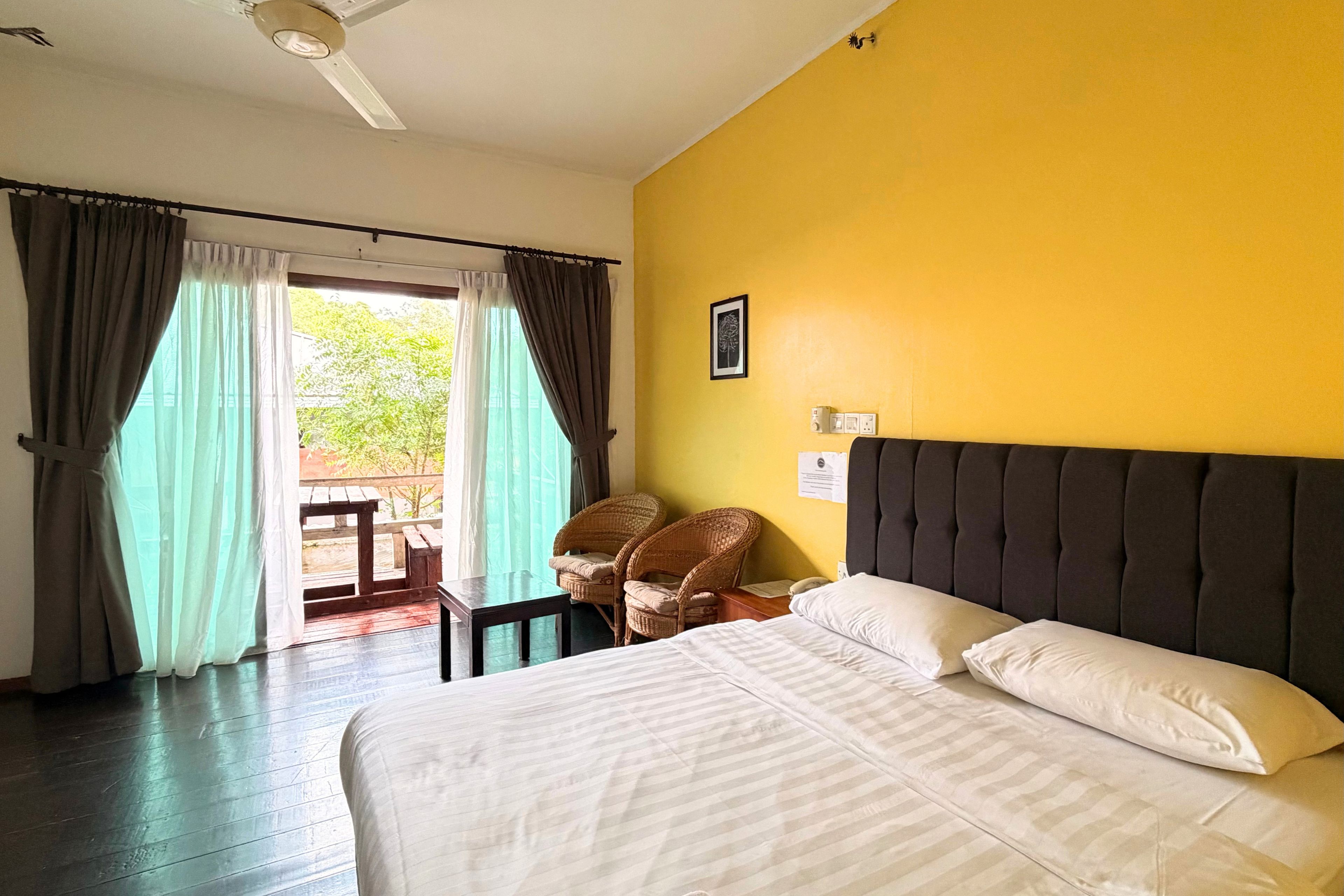 A hotel room with a bed, a chair, a window with curtains, and a ceiling fan.