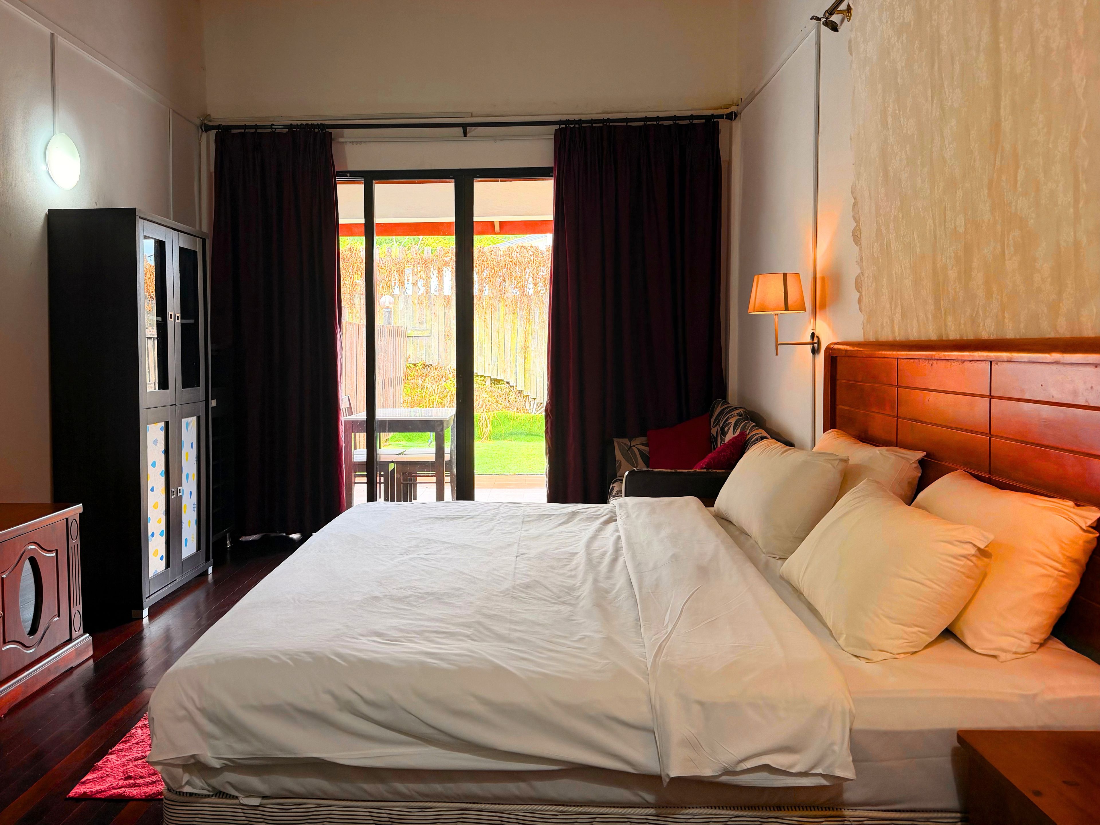A hotel room with a bed, a desk, a cabinet, and a view of the outside.
