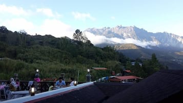 Un comedor con mesas y sillas, con vistas a un paisaje montañoso que incluye picos nevados y una colina boscosa.