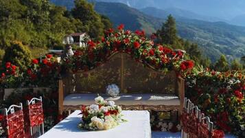 Montaje de ceremonia de boda con un banco decorado, arreglos florales y un paisaje montañoso de fondo.