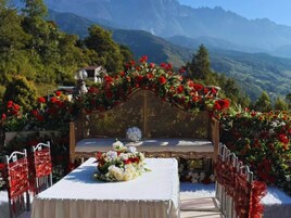 Preparação para uma cerimônia de casamento com um banco decorado, arranjos florais e uma paisagem montanhosa ao fundo.