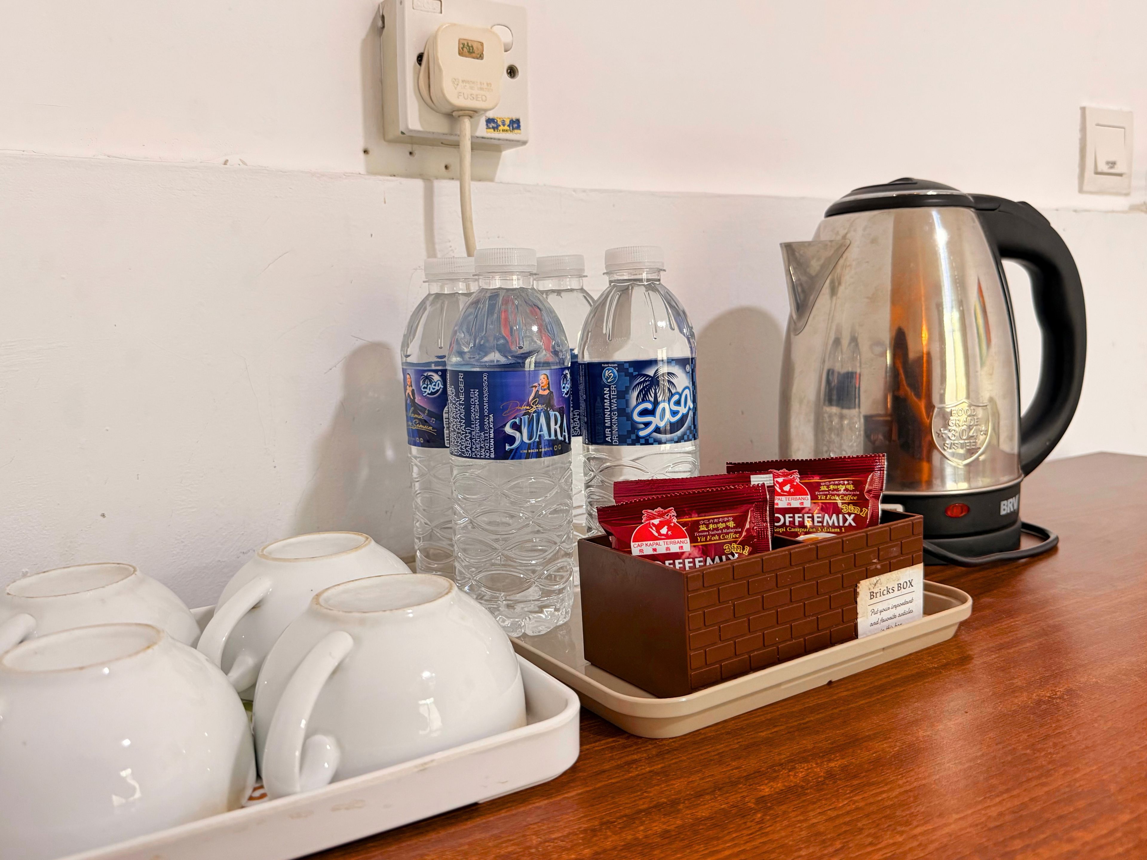 Un coin cuisine équipé d’une bouilloire, de deux bouteilles d’eau, d’un plateau avec des tasses à thé et d’une boîte de sachets de café.