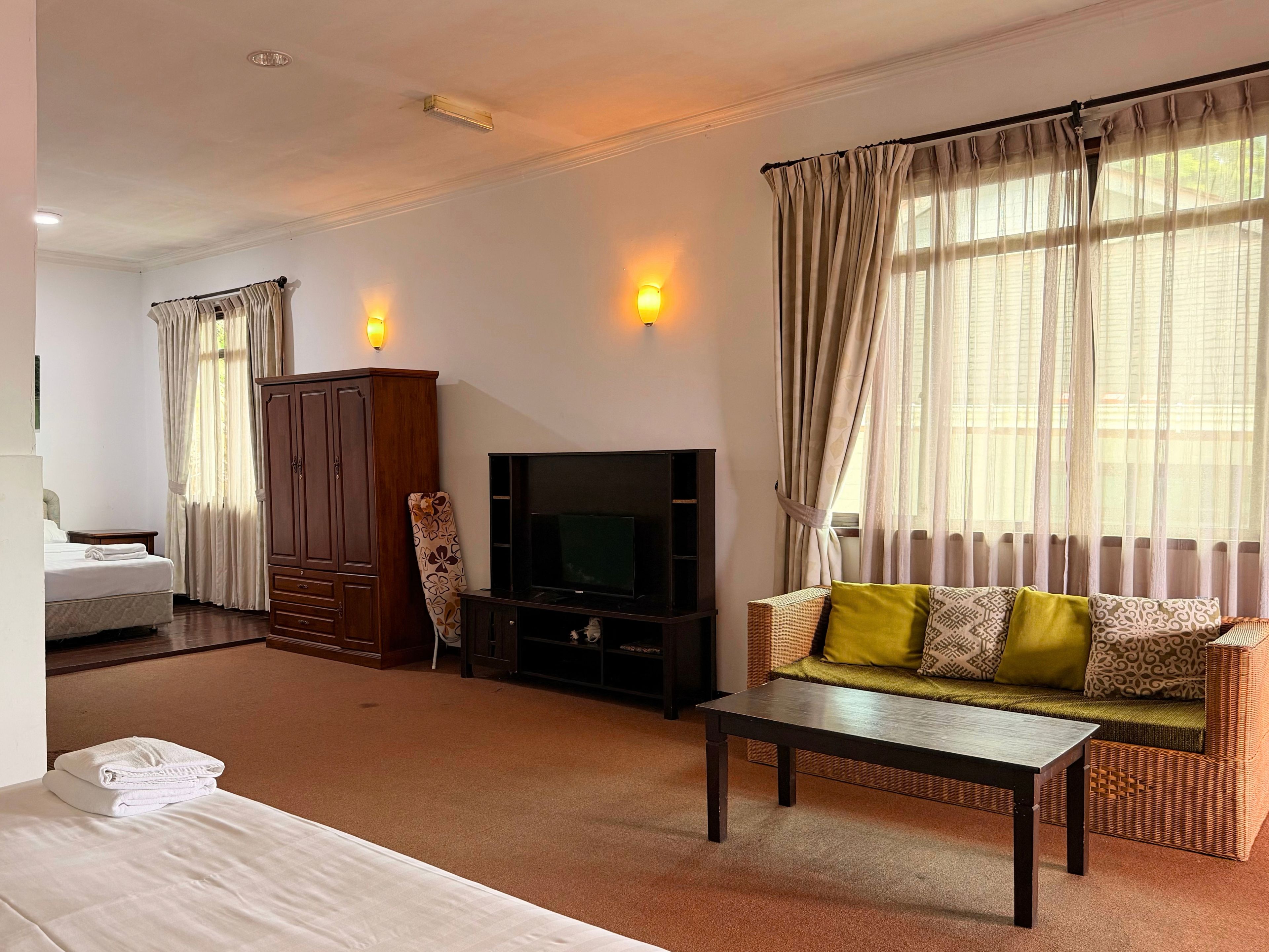 A hotel room with a bed, a television, a sofa, a cabinet, and a carpeted floor.