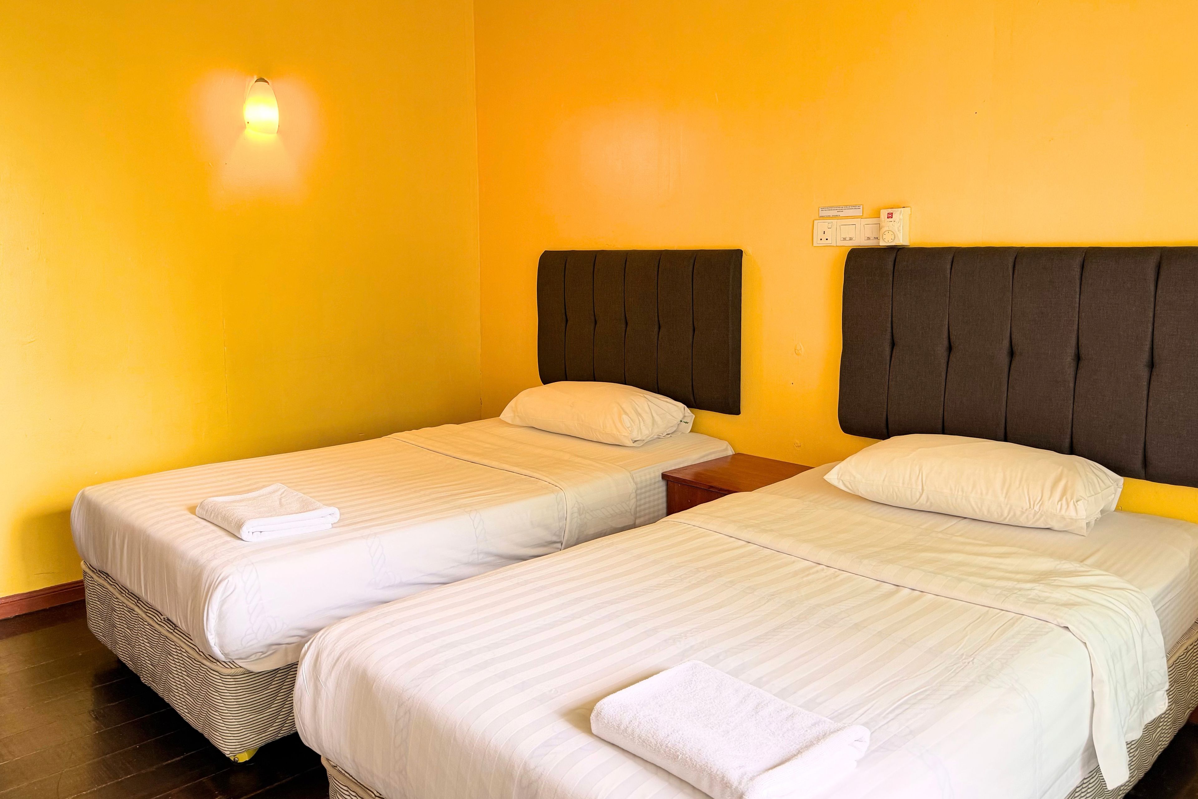 A hotel room with two single beds, each with a pillow and a folded towel.
