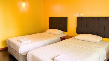 A hotel room with two single beds, each with a pillow and a folded towel.