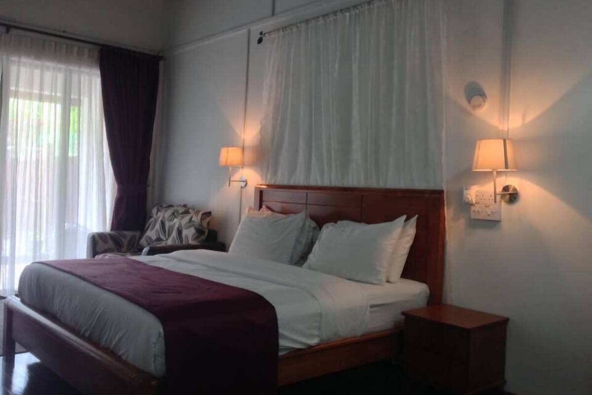 A hotel room with a large bed, two bedside lamps, a nightstand, and a window with curtains.