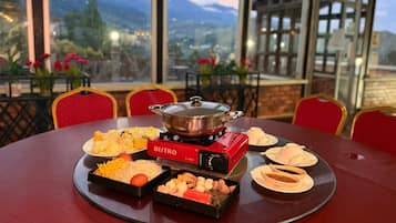 A dining table with a BISTRO brand portable stove, various dishes, and a scenic mountain view through large windows.