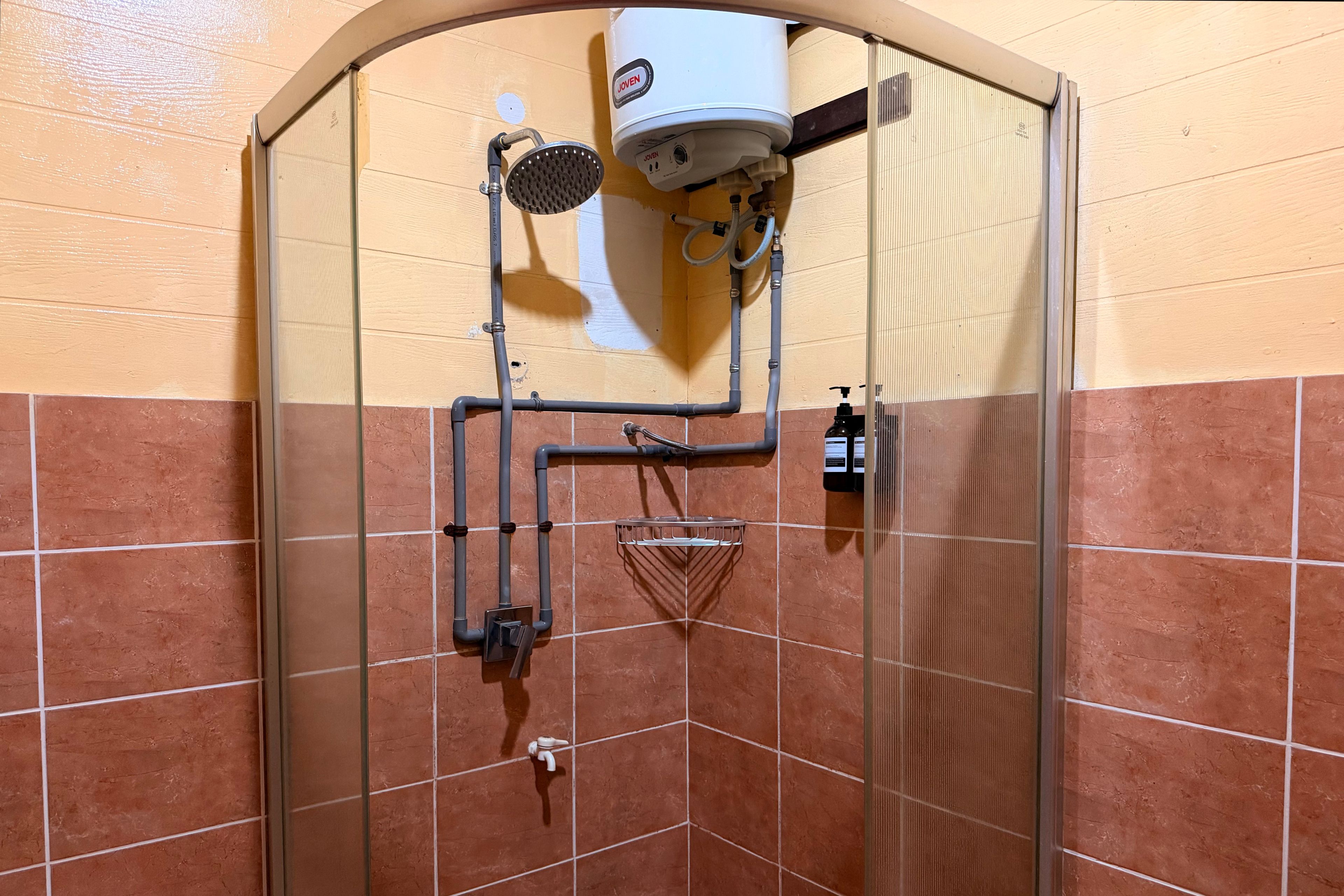 A shower enclosure with a glass door, a handheld showerhead, a wall-mounted control panel, and a handheld shower attachment.