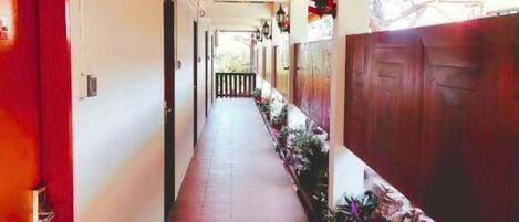 A corridor with a tiled floor, wooden doors, and a row of potted plants.