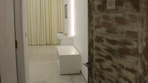 A hallway with a white door labeled '101', a white bench, and a window with curtains. - Heaven By O (Unawatuna)